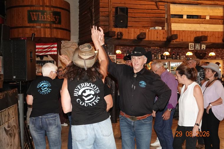 Dansers van Riverboots Country met de handen in de lucht op de dansvloer