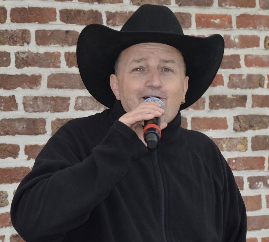 Patje Stew zingend met zwarte cowboyhoed voor een bakstenen muur